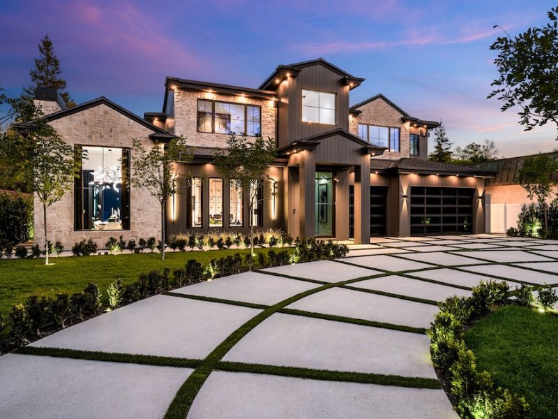 Modern luxury home exterior with a beautifully landscaped front yard and driveway at dusk.